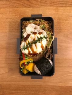 a bento box with noodles, vegetables and meats in it on a wooden table