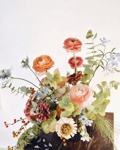 a vase filled with lots of flowers on top of a wooden table next to a white wall