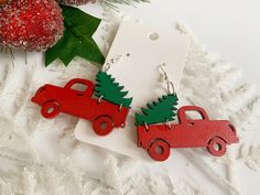 two red cars with christmas trees on them are sitting next to a pair of earrings