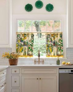 a kitchen with white cabinets and green floral valances on the window sill above the sink