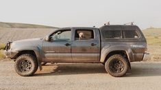 a gray truck parked on the side of a dirt road with a dog in it's bed