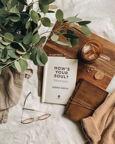 an open book sitting on top of a wooden table next to glasses and a potted plant