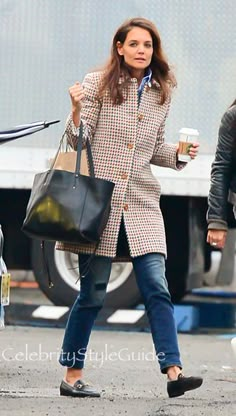 the woman is walking down the street with her hand in her pocket and holding a coffee