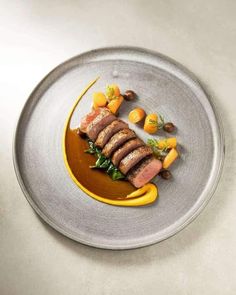 a plate with meat and vegetables on it, sitting on a white table top next to some oranges