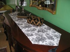 a table topped with a black and white cloth covered box on top of it next to a mirror