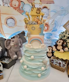 there are many stuffed animals sitting on top of this tiered cake that is decorated with an elephant, giraffe, monkey and rainbow