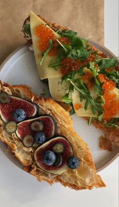 a white plate topped with two pieces of bread covered in fruit and veggies