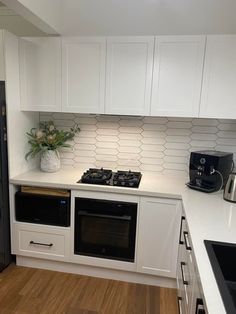 a kitchen with white cabinets and an oven in the center is seen from across the room