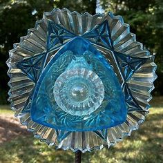 a blue glass sun catcher sitting on top of a wooden stand in the grass next to trees