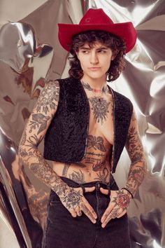 a man with tattoos and a red hat standing in front of a silver sheeted wall