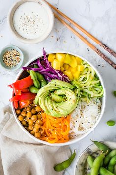 a white bowl filled with vegetables and rice next to chopsticks on the side