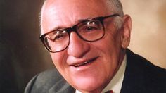 an older man with glasses and a bow tie smiling at the camera while wearing a suit