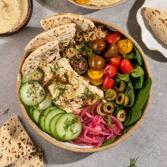 a bowl filled with different types of vegetables and pita bread on top of a table