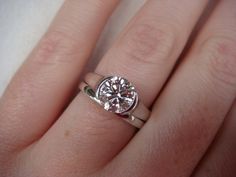 a woman's hand with a diamond ring on top of her finger, showing the center stone