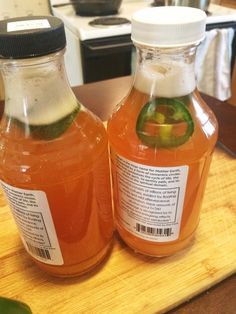 two bottles of liquid sitting on top of a wooden table next to a green pepper