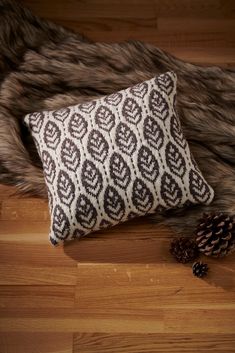 a black and white pillow sitting on top of a wooden floor next to a pine cone