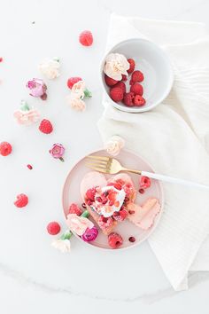 a heart shaped cake on a plate with raspberries and whipped cream around it