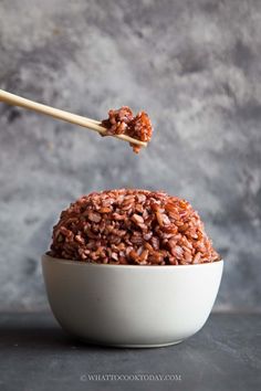 a white bowl filled with brown rice and chopsticks sticking out of the top