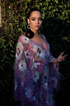 a woman in a purple dress standing next to a bush