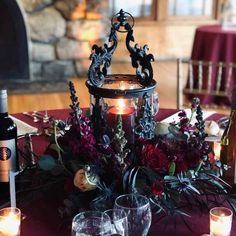 a table with candles, flowers and wine bottles on it in front of a fireplace