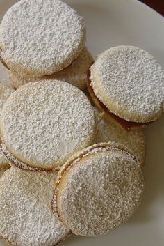 a white plate topped with cookies covered in powdered sugar on top of a wooden table