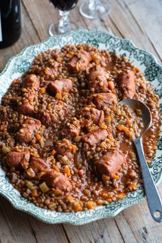 a plate full of meat and beans on a wooden table with wine glasses in the background