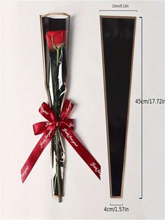 a red rose in a box with a ribbon tied around it next to a black piece of cardboard