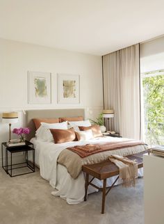 a bedroom with white walls and beige bedding, two pictures on the wall above the bed