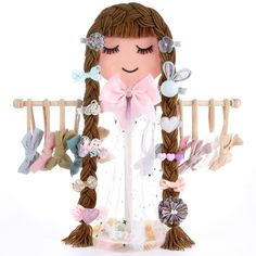 a doll with long brown hair wearing a pink bow and holding a wooden clothes rack