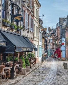 a cobblestone street with tables and chairs on the sidewalk in front of buildings