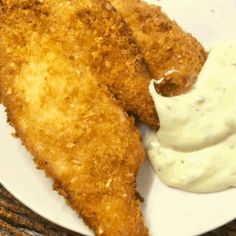 two pieces of fried fish on a white plate with sour cream and mayonnaise