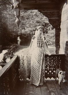 an old black and white photo of a woman in a long dress standing on a porch