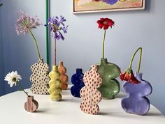 five colorful vases with flowers in them on a white table next to a blue wall