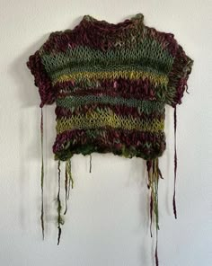 a knitted sweater hanging on the wall next to a white wall with green and red yarn