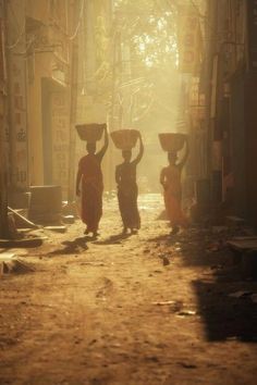 three people carrying baskets on their heads down a street