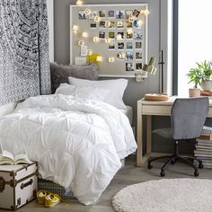 a bed with white comforter and pillows next to a desk in front of a window