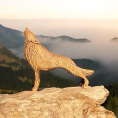 a wooden carving of a dog standing on top of a rock with mountains in the background