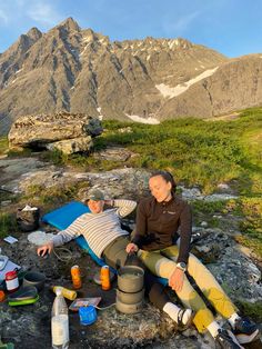 two people sitting on top of a mountain next to each other with camping equipment around them