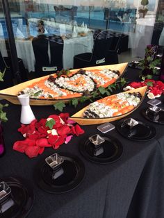 two pizzas with toppings sit on black plates next to red and white flowers