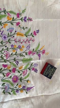 an embroidered table cloth with flowers and leaves on it, next to a small book