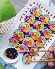 a person is holding chopsticks near some food on a white platter with colorful powdered donuts and dipping sauce