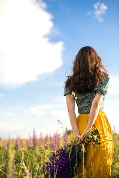 a woman in a yellow dress is standing in the middle of a field with purple flowers