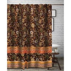 a brown shower curtain with an orange and yellow flower design on it, in front of a white brick wall