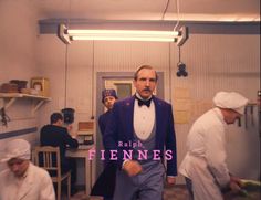 a man in a tuxedo and bow tie standing in a kitchen with other men