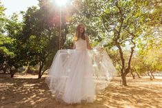 a woman in a white dress standing under trees