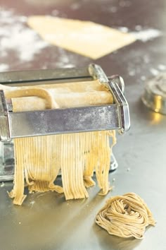 a close up of a pasta machine with some noodles on the ground next to it