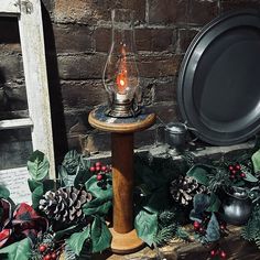 an old fashioned lamp is sitting on a table surrounded by greenery and pine cones