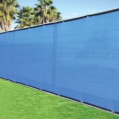 a large blue privacy fence in the middle of a grassy area with palm trees behind it