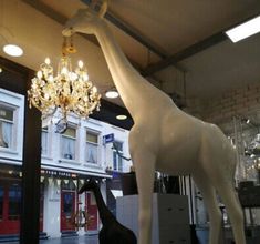 a giraffe statue in front of a store window with a chandelier hanging from it's ceiling