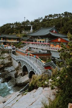 a bridge over the water in front of some buildings on top of a cliff next to the ocean